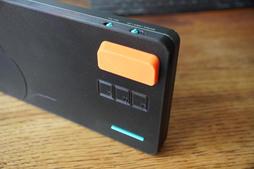 the back edge of the assembled base, with three square debug access ports below an orange flip-out foot and the two teal mode switches above