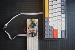an Arduino Nano on a breadboard, wired through jumper wires and a ribbon cable to a NuPhy Air60 next to it