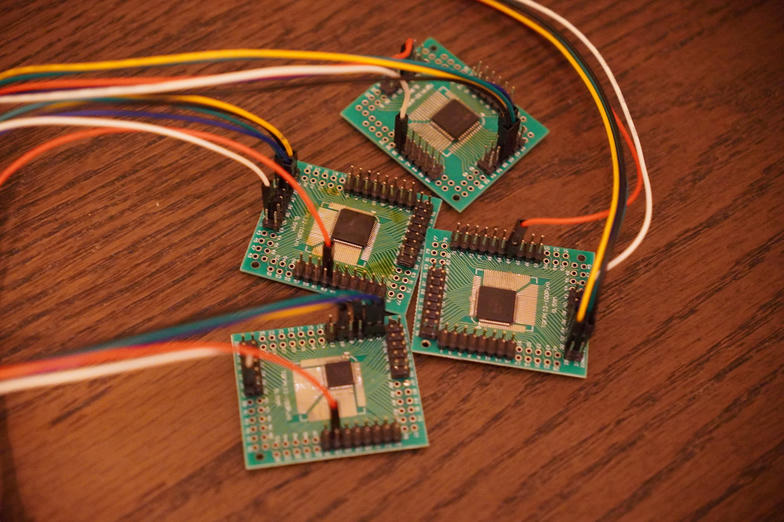 four green breakout boards on a wooden desk, each with a bare Sinowealth QFP chip soldered in the middle and jumper wires running off the pin headers